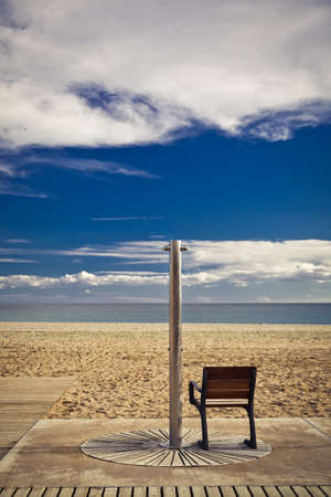 Aluminum shower with wooden seat for disabled people; sand beach, sea, horizon and blue sky with white clouds on the backgroundの写真素材