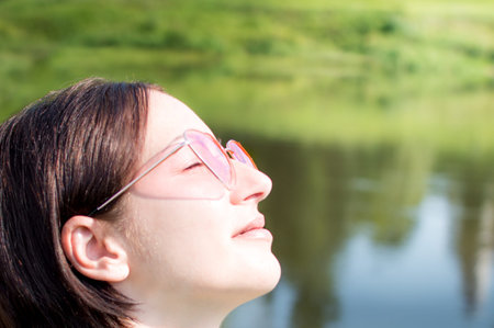 close-up portrait of a young woman in the sun in sunny pink glasses and eyes closed