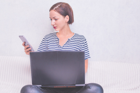 Young woman on bed with laptop and phone. Concept of modern technology and devices.の写真素材