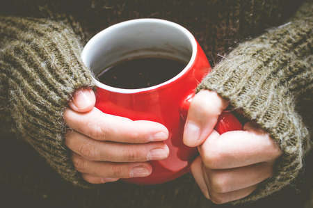 Red cup with coffee in the hands of a woman in a wool sweaterの写真素材