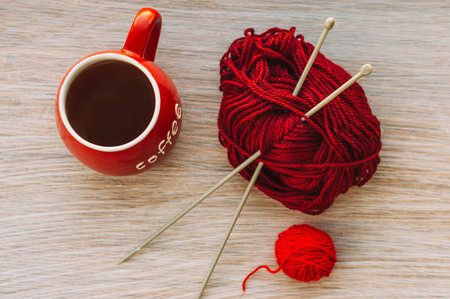 Two tangle of yarn for knitting on the table. There is a red cup with an inscription of coffee.