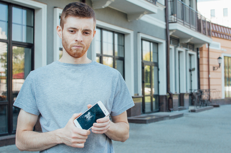 Man holds a mobile phone with a broken screen in his hands on the street.の写真素材
