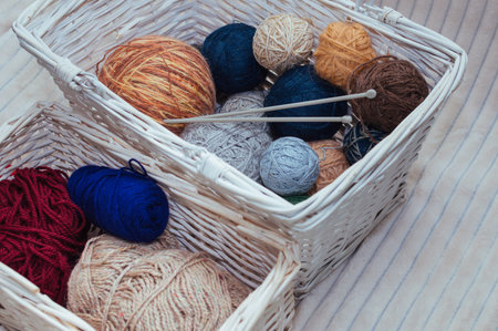 Multicolored balls of yarn and knitting needles in a white basket. Concept storage of yarn and...