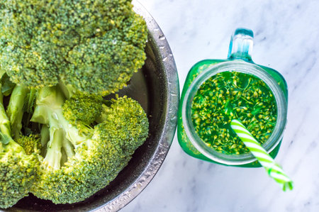 Green smoothie with straw and iron bowl with broccoli. Closeup