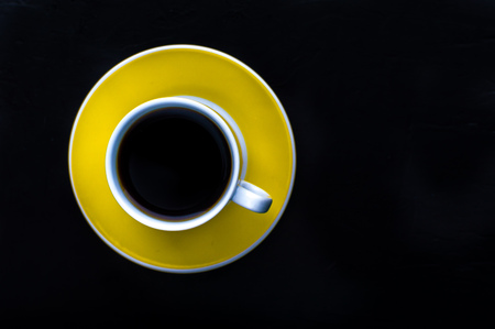 Yellow cup of coffee on a black background. Minimalism. Top viewの写真素材