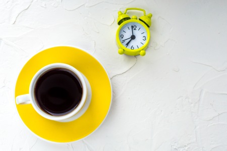 Yellow cup of coffee and an alarm clock on a white background. Minimalism. Concept morningの写真素材