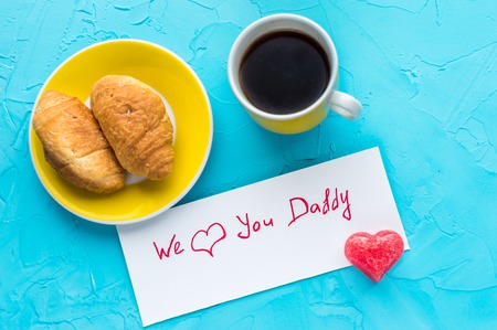 Father's day concept.Text we love dad. Close up.Croissants and a cup of coffee with congratulations for father on holiday. Father's day concept.Text we love dad.Blue backgrounds.の写真素材