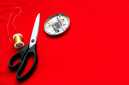 Scissors for cutting, needles and thread on a red cloth. Concept design clothes.