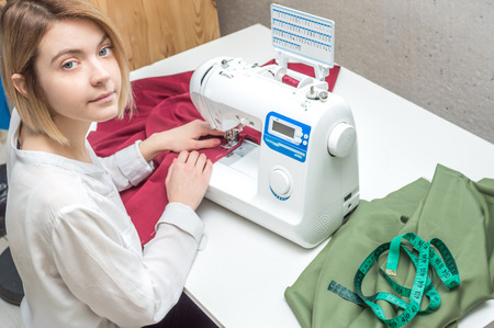 young woman sews clothes on a sewing machine. Closeup portraitの写真素材
