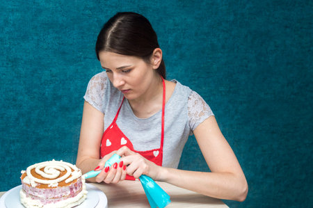 Housewife puts cream on sponge cake in the kitchen.