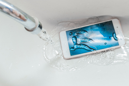Smartphone dropped into the sink under the water. Concept mobile phone repair. Recessed phone into the water.の写真素材