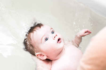 Baby bathes in the bath. Dad holds the baby in the water. Close up portrait