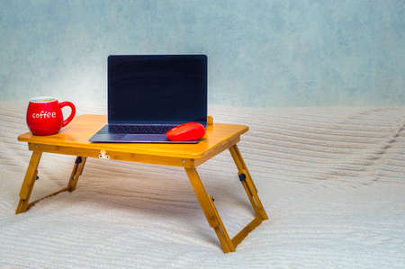 laptop and a computer mouse on a laptop stand and cup of coffee on a bed. Concept working remotely. Copy spaceの写真素材