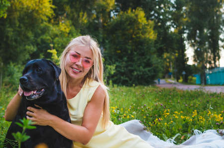 Portrait of a young beautiful girl with white hair with a black dog in the parkの写真素材