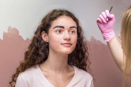 eyebrow master draws the shape of the eyebrows of a young woman with an eyebrow pencil. Henna eyebrow coloring procedure in a beauty salonの写真素材