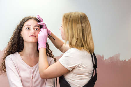 eyebrow master draws the shape of the eyebrows of a young woman with an eyebrow pencil. Henna eyebrow coloring procedure in a beauty salonの写真素材