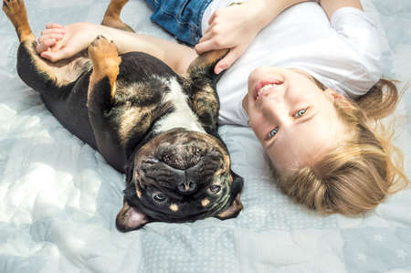 girl lies on the bed in an embrace with her dog of the French Bulldog breedの写真素材