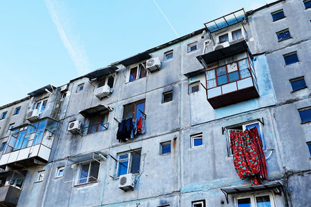 A worn building stands in a city with many windows and a few air conditioning units. Some clothes...