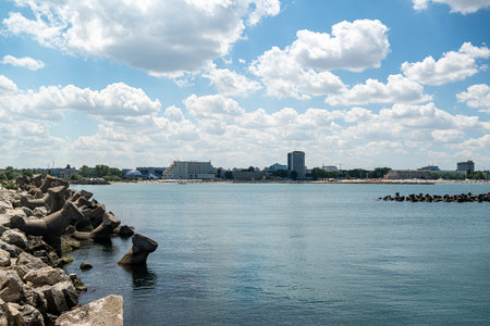 The scene shows a city next to water with rocks along the shore. Clouds fill the sky above....