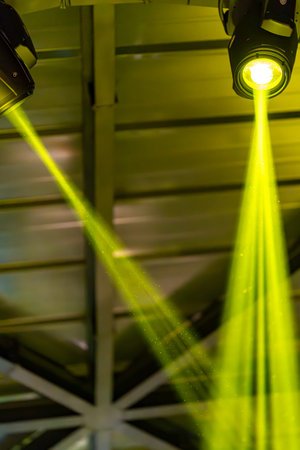 Bright beams of green light are directed down from stage lights in a venue. The lights create a vibrant atmosphere during an event. People enjoy the show.の写真素材