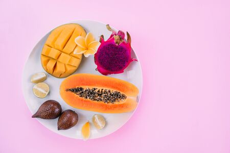 Papaya, mango, dragon fruit, snake fruits and lime on plate on pink background. Tropical flat lay. Food concept.の写真素材