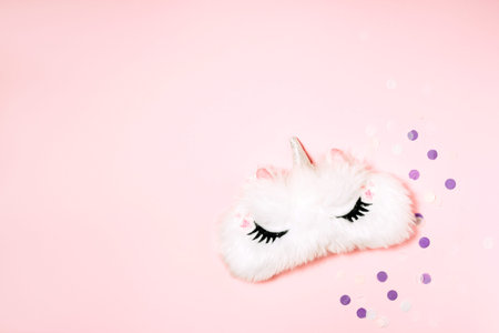 Flat lay photo of unicorn sleep mask on pink background with festive confetti. Top view, space for...