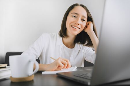 Happy young woman sitting at the table and using laptop, calling by video chat.の写真素材