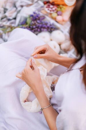 Hands close-up knitting on knitting needles, white milk wool knit during a picnic. Needlework in the garden.の写真素材