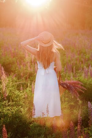 Girl with long hair standing with his back at sunset with a large bouquet of lupins.の写真素材