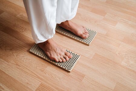 Close-up of unrecognizable brave man in white pants standing barefeet on bed of nails at morning yoga practice. Balance exercise, courage and patience.の写真素材