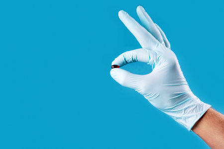 Small pill in the hand in medical gloved palm on neo mint color background. Concept of coronavirus and Covid-19.の写真素材