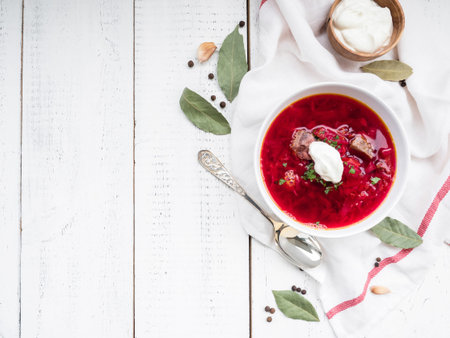 Red borscht soup in white bowl with sour cream, top view, isolated on wooden background.