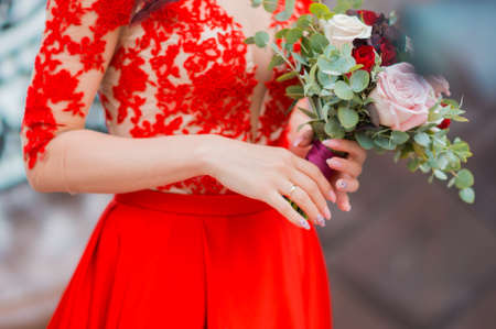 The bride in red wedding dress is holding bouquet of rosesの写真素材