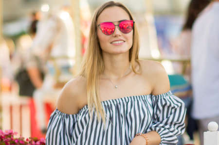 Portrait of a young woman in red sunglasses on a bright background. Beautiful summer girl on the background of a merry-go-round.の写真素材