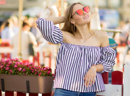 A girl in bright red glasses stroking her hair against the backdrop of a carousel. Summer portrait of a girl on a bright backgroundの写真素材