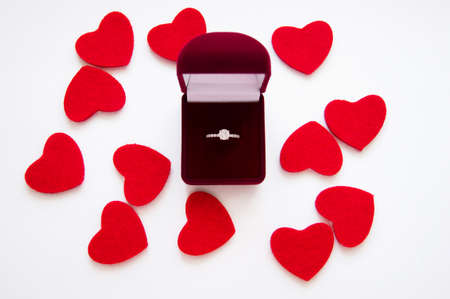 Top view of beautiful luxury wedding ring with precious stone in red velvet gift box on white backgroung with red hearts. Valentine's day marriage proposal. Present and love concept.の写真素材