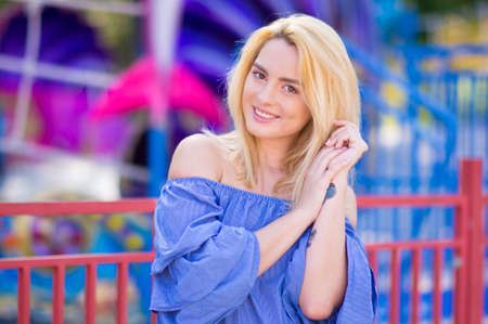 Beautiful young woman with blond hair smiling on a bright background of blurred amusement parkの写真素材