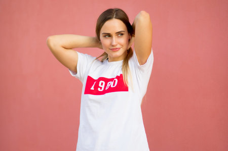 Simple portrait of a girl with blond hair in casual white t-shirt gathering hair on pink background