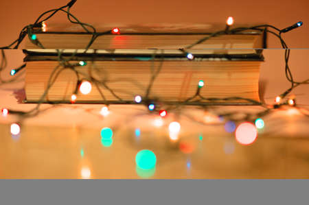 Stack of two books with garland on pink background and defocused garland lights bokeh in the foreground. Reading and education concept. Reading for girls concept. Decorations on christmas and new year holidays for cozy home interior.の写真素材