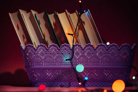 Books in basket and colorful garland on the dark. Garland lights bokeh in the foreground. Decorations for cozy home interiorの写真素材