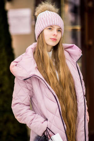 A girl with long blond hair in a pink warm jacket and hat with 
pompon stands on the background of golden doors. Winter wonderland. Christmas and New Year concept.の写真素材