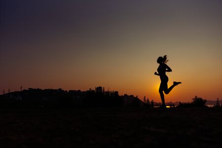 The woman does exercises at sunrise. Morning warm-up. A silhouette against the background of a rising sunの写真素材