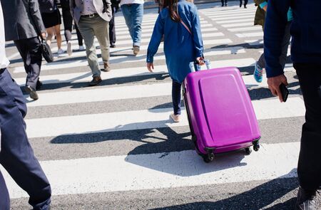 the girl drags a suitcase on wheels on the crosswalkの写真素材