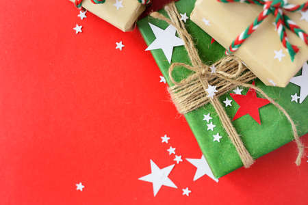 The Christmas gifts packed into a beige and green kraft paper, strewed with red, white paper stars on red background. Top View Flat Layの写真素材
