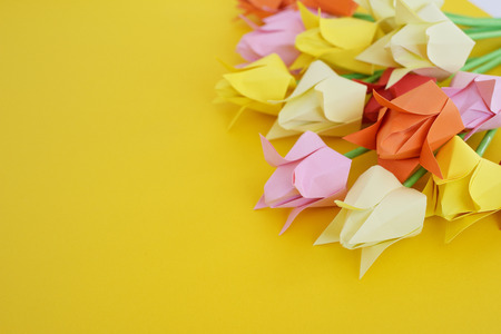 Tulips of origami from multi-colored  paper on a yellow backgroundの写真素材