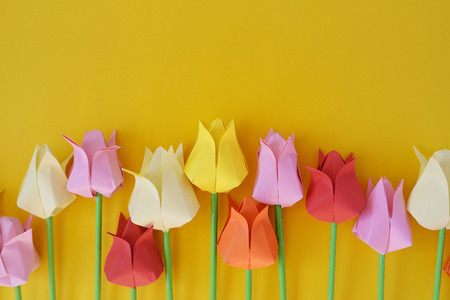 Tulips of origami from multi-colored  paper on a yellow backgroundの写真素材