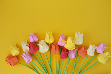 Tulips of origami from multi-colored  paper on a yellow backgroundの写真素材