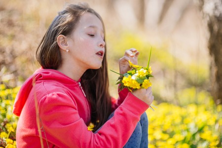 The lovely girl of years of eight walks in the spring wood, collects the first spring flowersの写真素材