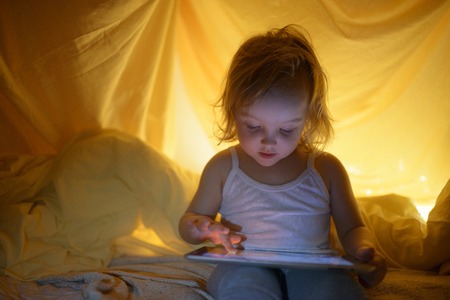 Two kids using tablet pc under blanket at night.の写真素材