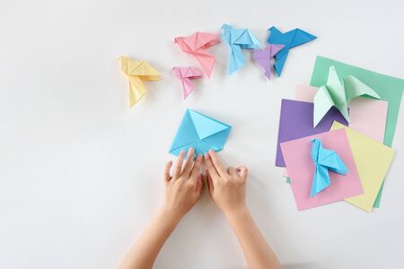 Children's hands do origami from colored paper on white background. lesson of origamiの写真素材